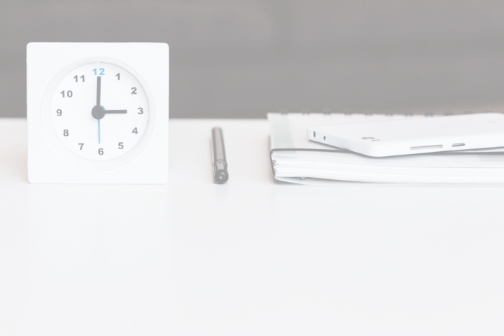 A desk clock beside a pen and a notebook