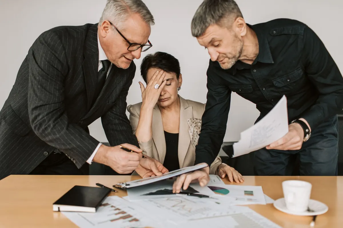 Distressed employee at a desk while two male colleagues lean over her